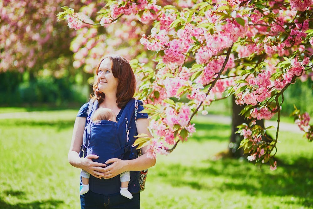 A woman enjoying outdoors with her baby in a baby carrier
