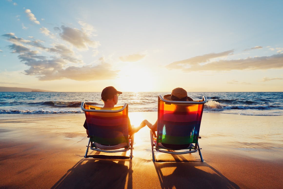 two people sitting in chair on the beach watching sunset