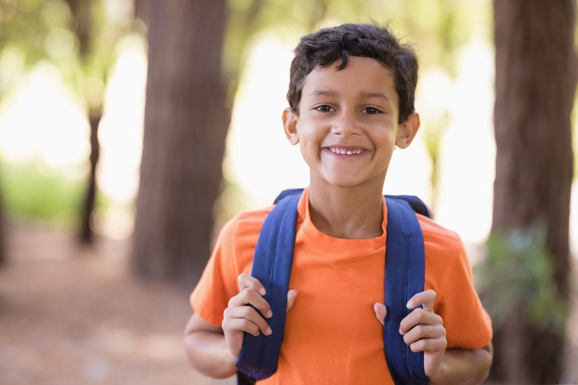 little boy wearing a backpack and orange shirt