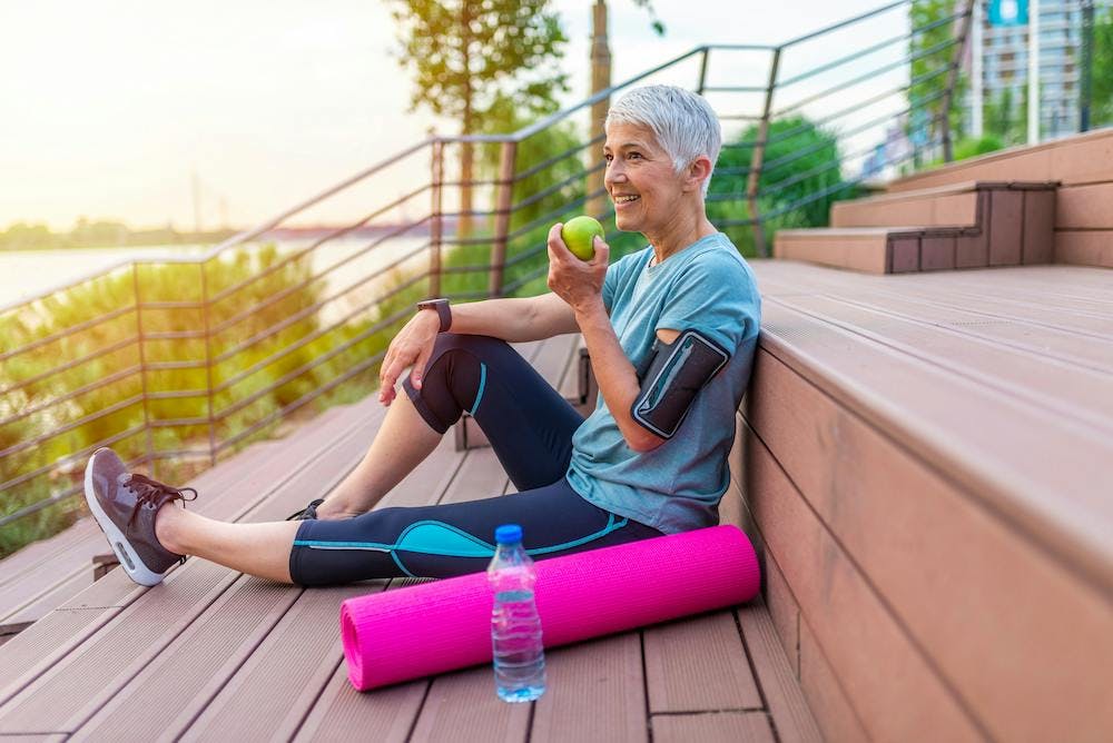 older woman with yoga mat and apple